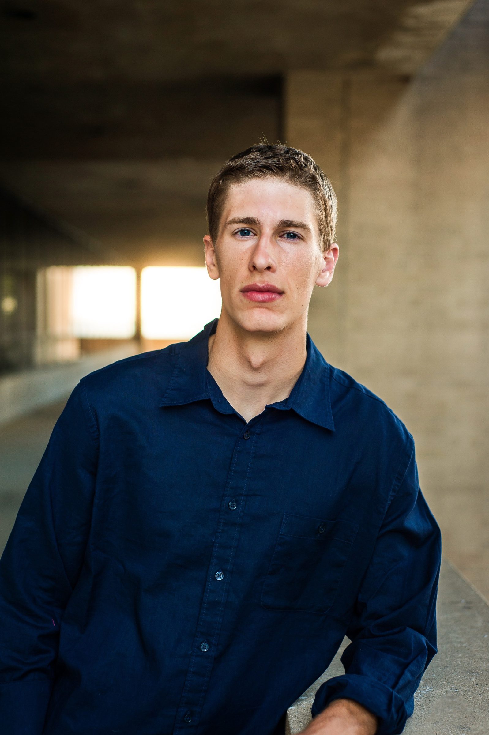 A young man in a navy shirt standing in a concrete underpass, lit softly from the side.